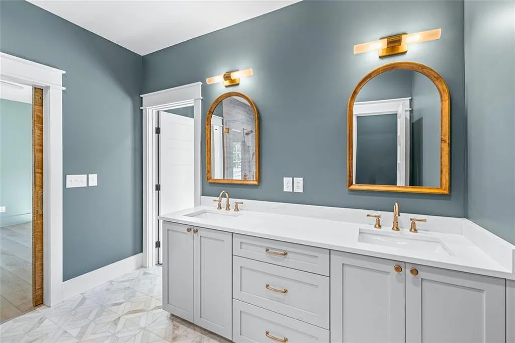 Bathroom remodel with blue-gray walls, arched mirrors, and double vanity with gold fixtures